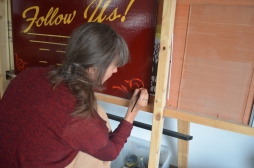 Rima paints scrolls in the corners of the signboards